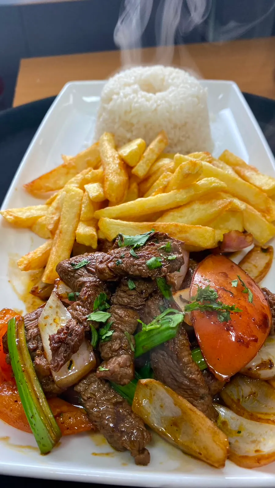 Lomo saltado humeante con arroz y papas fritas